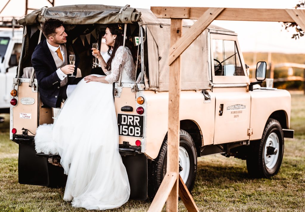 Bride and groom having a champagne in a car land rover