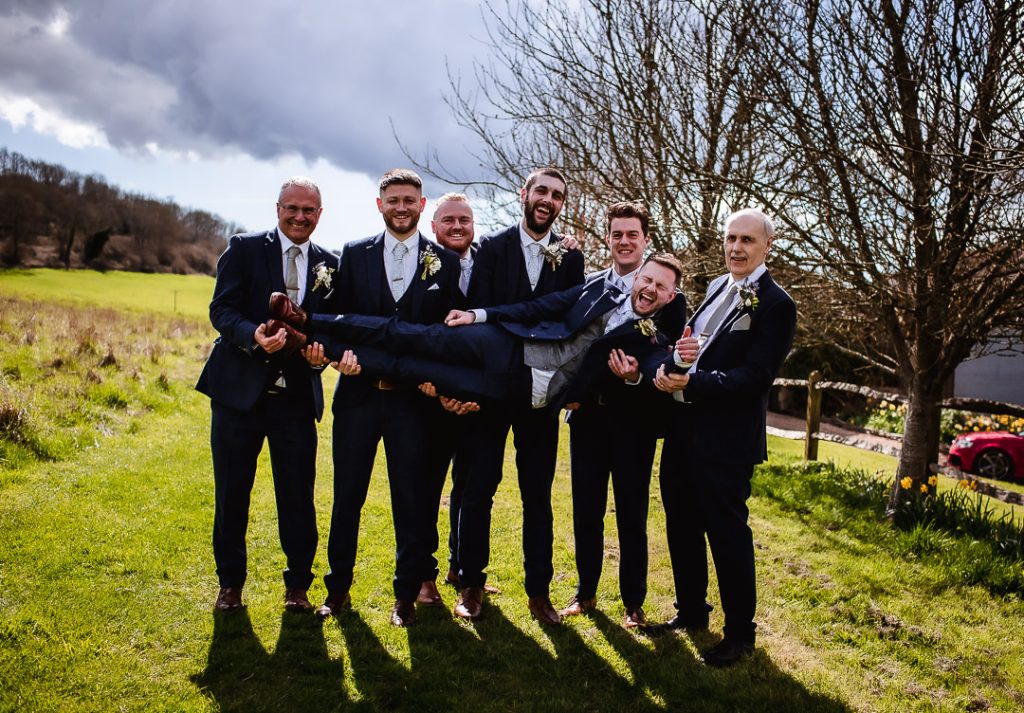 fun group photos with groomsmen holding a groom in the field