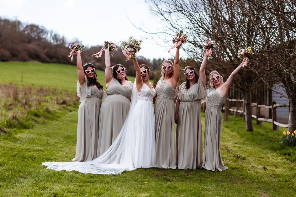 bride and bridesmaids in the field with heart sunglasses and flowers