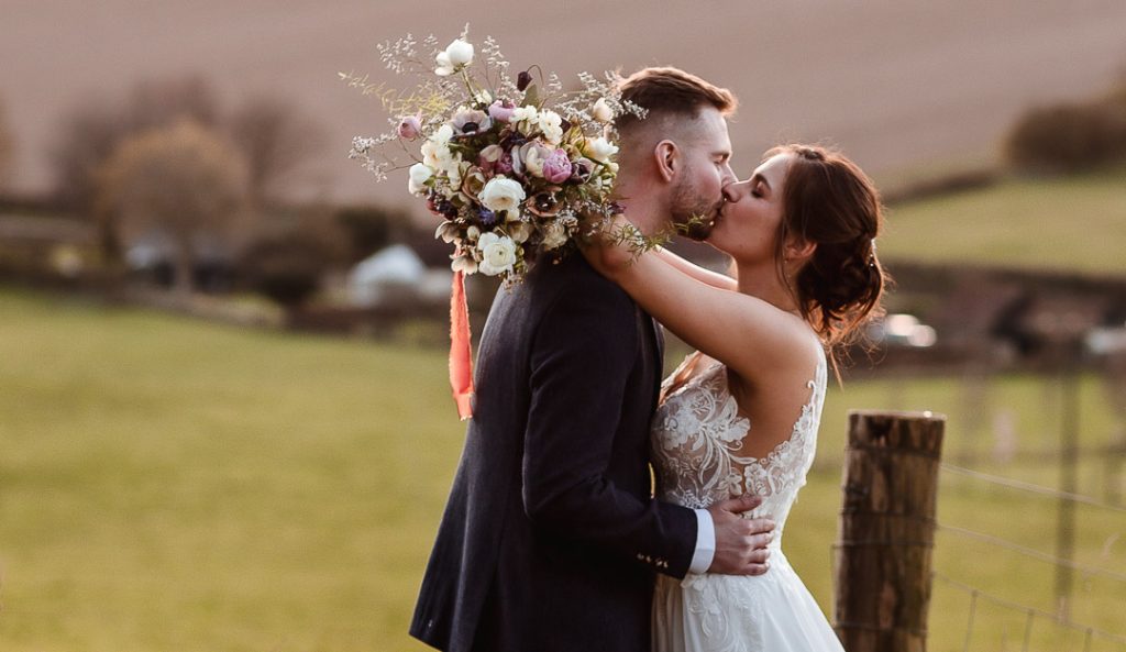 Bride and groom kissing in the field during the sunset