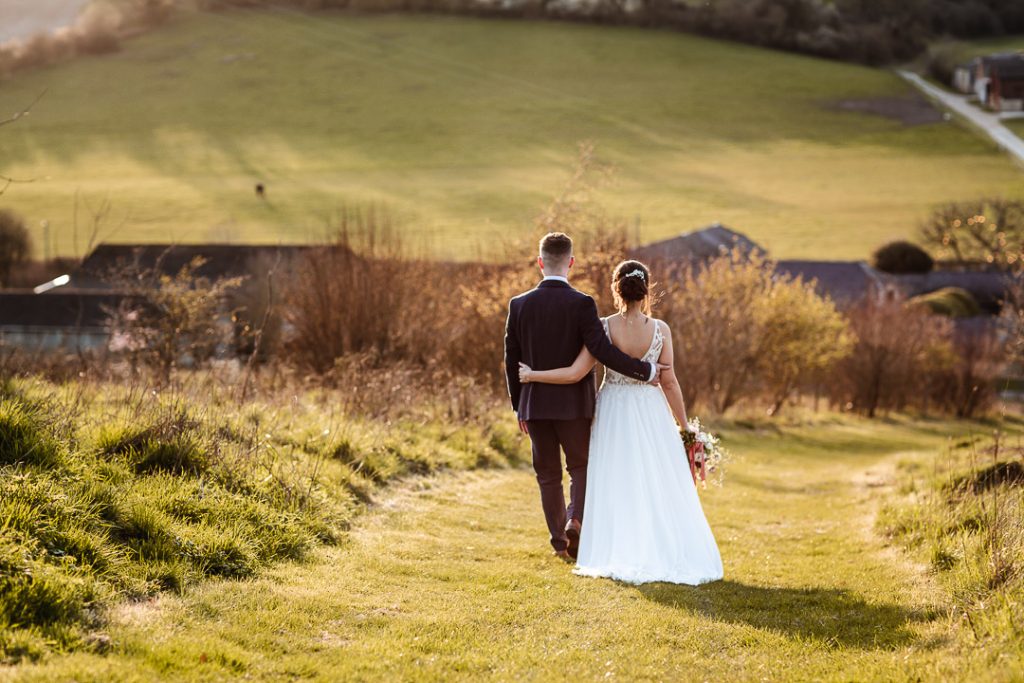 natural sunset photo of wedding couple walking in the field. Bride and groom on the hill with a beautiful countryside view