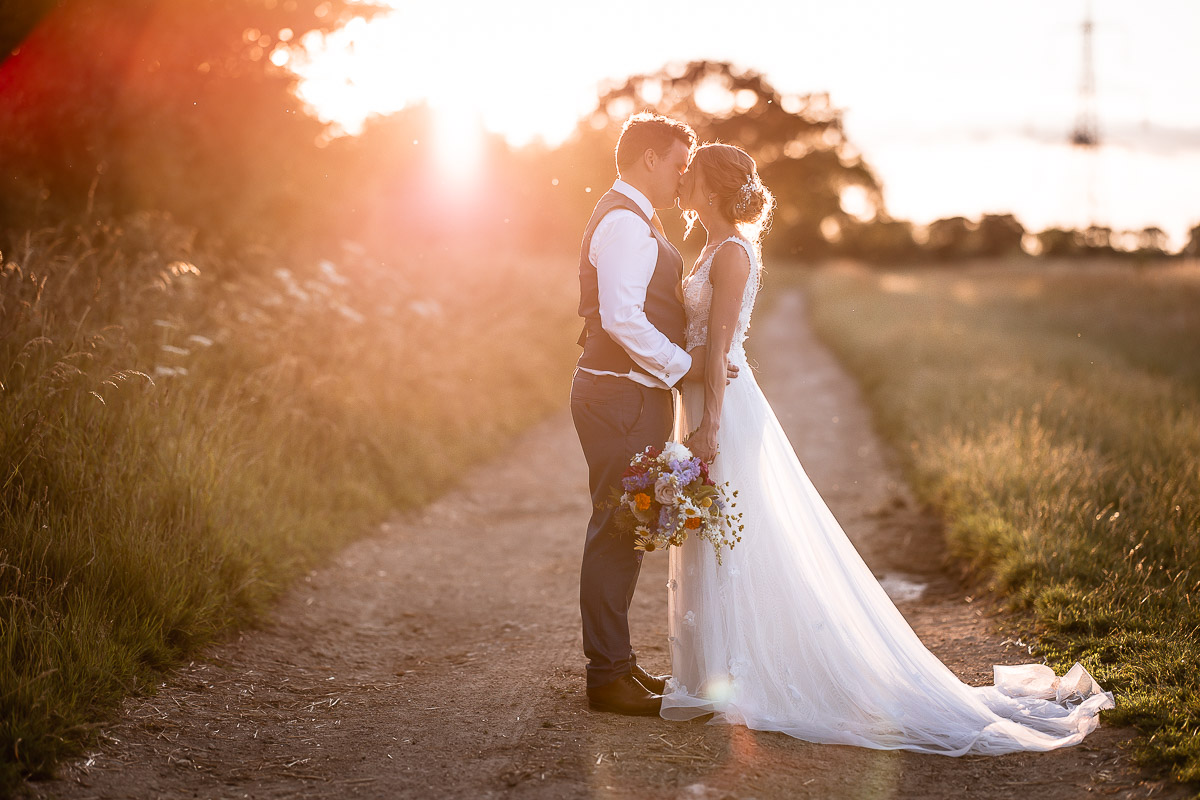 sunset photo of bride and groom kissing in the countryside