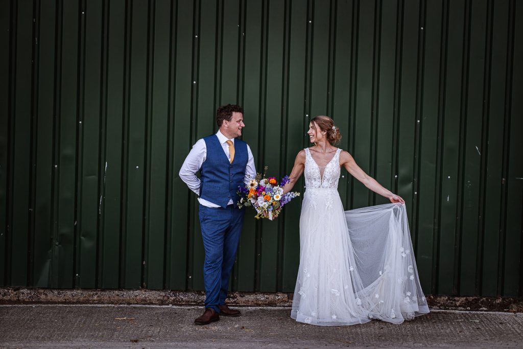 Photo of bride and groom standing in front of green rustic gate holing their hands and looking at each other