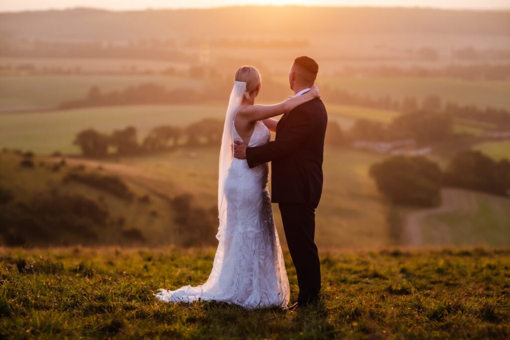 Sunset wedding photo of bride and groom on the top of the hill in the field