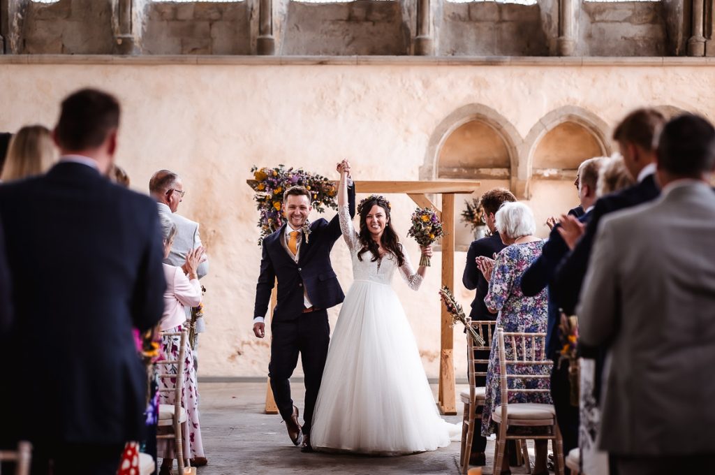 happy bride and groom exiting the aisle with cheering guests. West Sussex wedding photograher