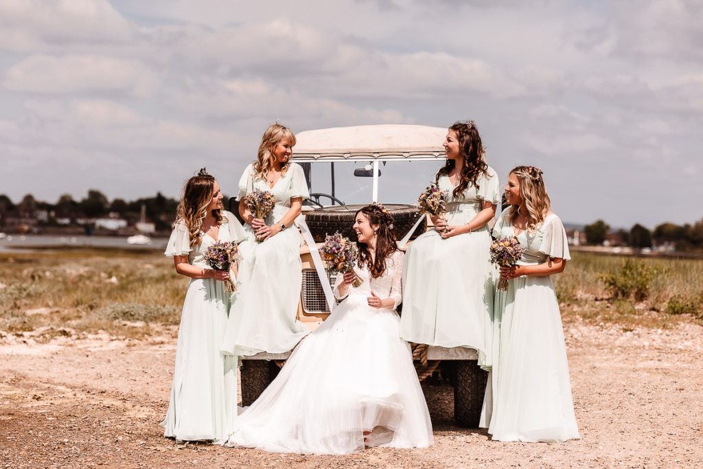 bride and bridesmaids siting on a land rover by harbour at West Sussex