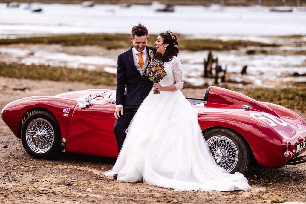 bride and groom are laughing and sitting on a car. Bosham wedding photographer at Harbour in Sussex