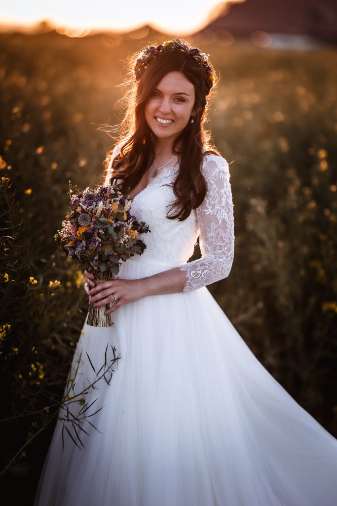 magical sunset photos of bride in the field holding her flowers. Bridal portrait in glowing sunset at Chidham Barn