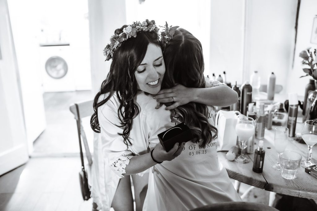 Bride and her bridesmaid is getting ready in the cottage. Emotional photo of bride and her sister