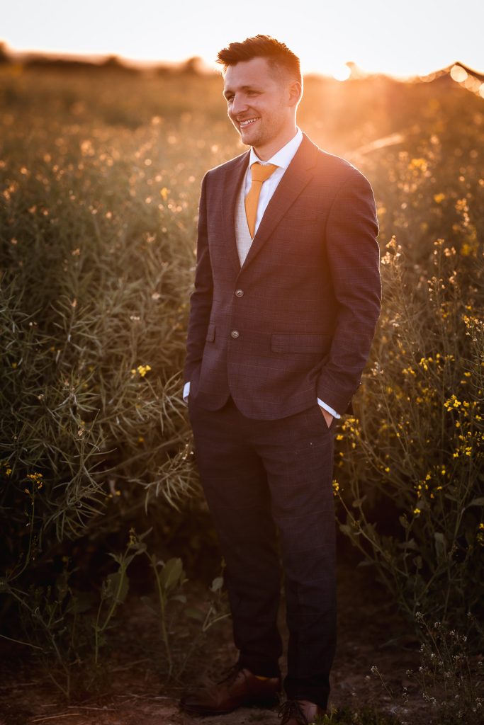 magical sunset photos of groom in the field with his hands in the pockets