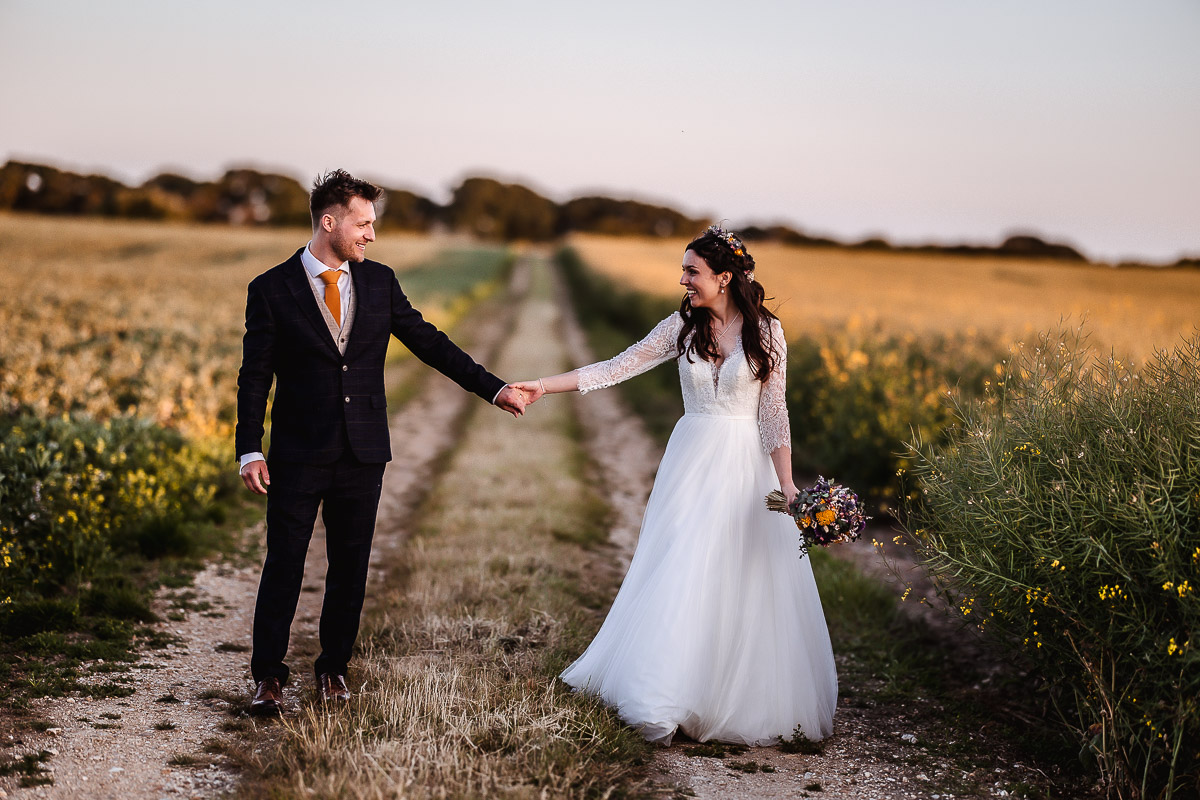 wedding summer photo of bride and groom walking in the field during the sumset at Chidham Barn Chichester