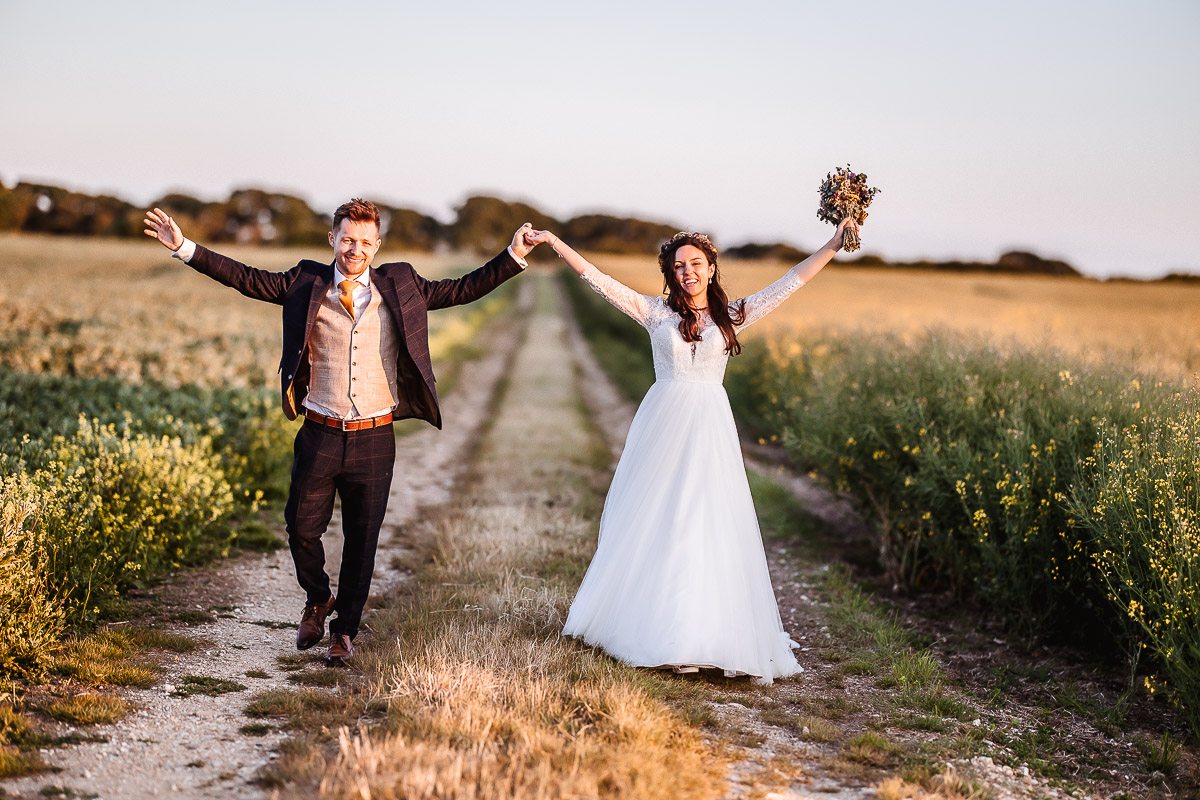 happy bride and groom waling in the filed with their hands up