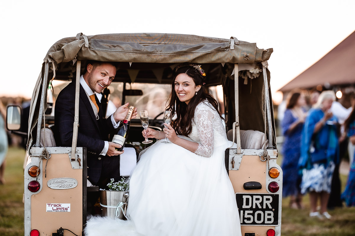 bride and groom having a prosecco in the land rover at Chidham Barn