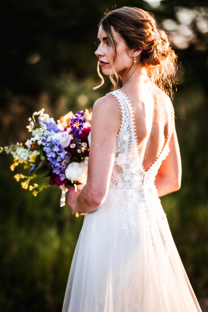 Romantic portrait of bride standing in the field and holding her flowers at OXLEAZE BARN COTSWOLD