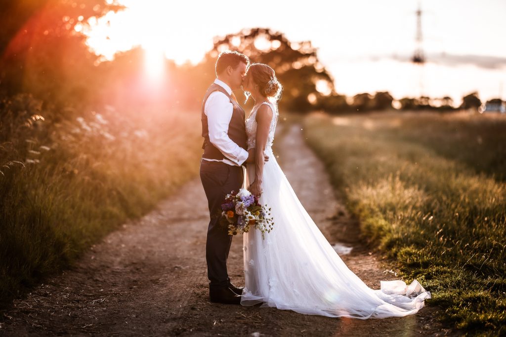 Sunset photo of bride and groom kissing on the pathway at Oxleaze Barn Cotswold.