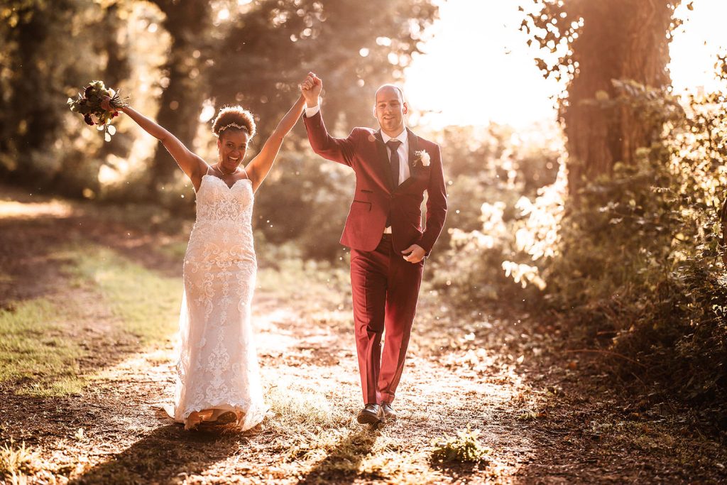 Sunset photo of happy bride and groom walking with their hand up in the air in the woods of Tournerbury, Hayling Island wedding photographer