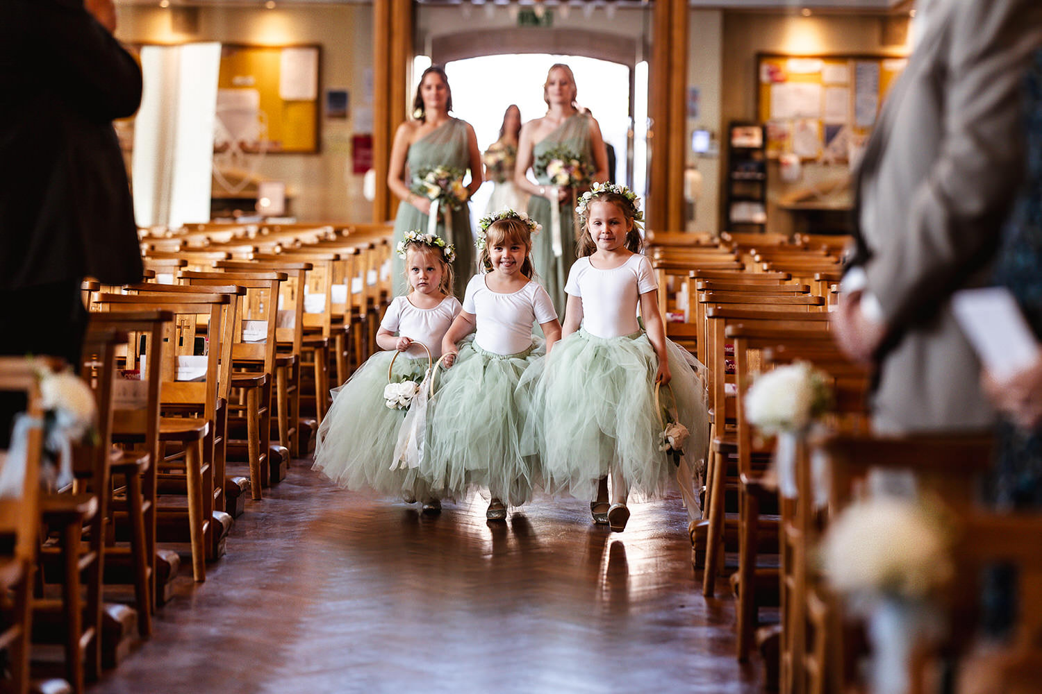 three flower girls with green skirts walking down the isle at the church in Chichester wedding