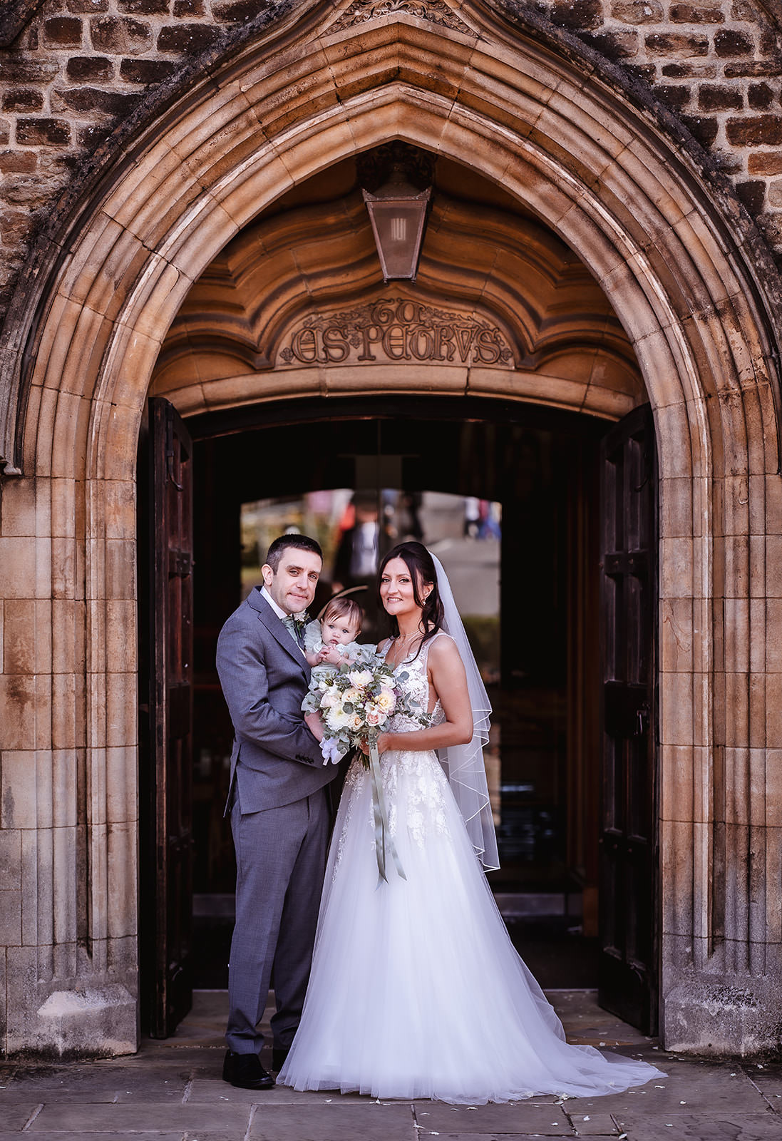 portrait photo of bride and groom and their baby outside of the church in Chichester