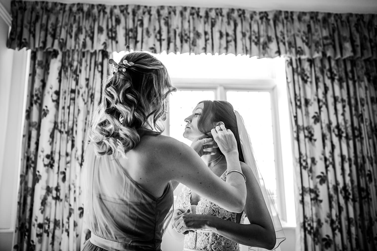 black and white photo of bride putting her earrings on by the window. Winchester wedding photography