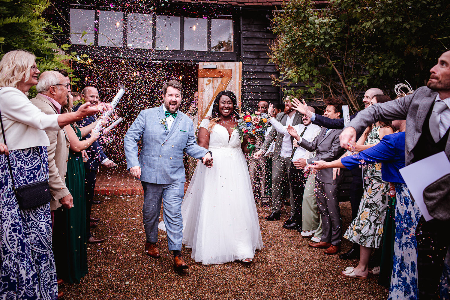 fun and colourful wedding confetti photo of bride and groom at High Billinghurst Farm. Surrey wedding photography