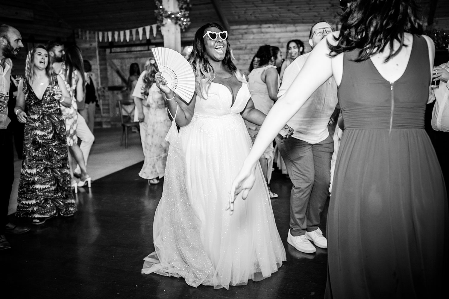 black and white photo of bride dancing with her heart shape sunglasses at High Billinghurst Farm