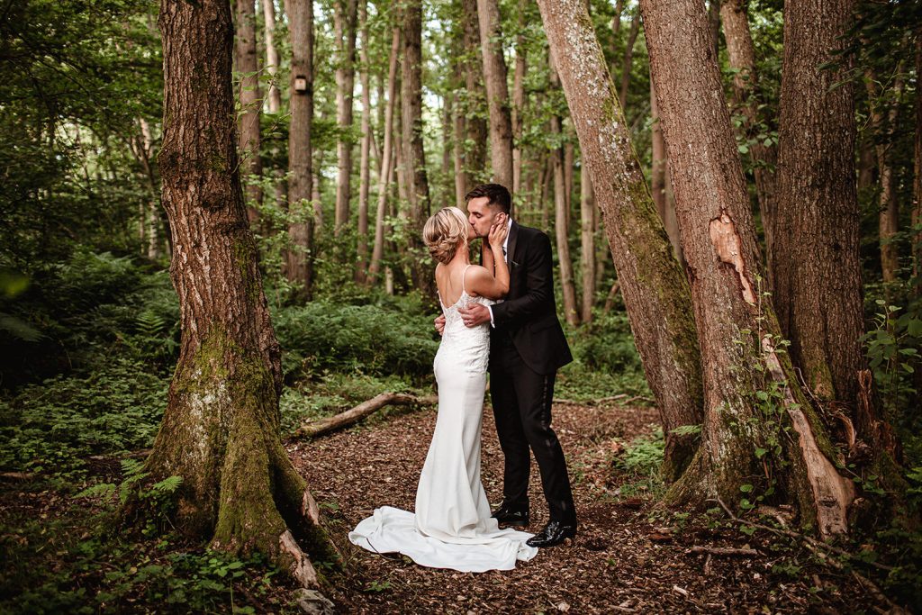 bride and groom are kissing in the forest/woods at Surrey wedding venue in Guildford