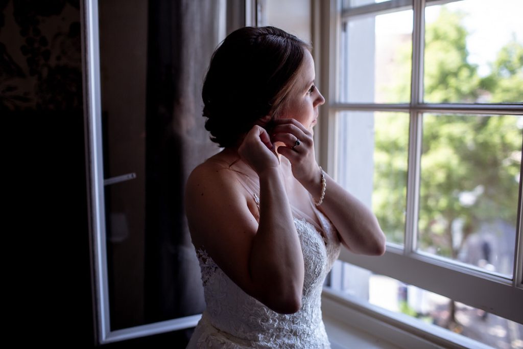 Bride is getting ready putting her earrings by the window at Hampshire wedding 