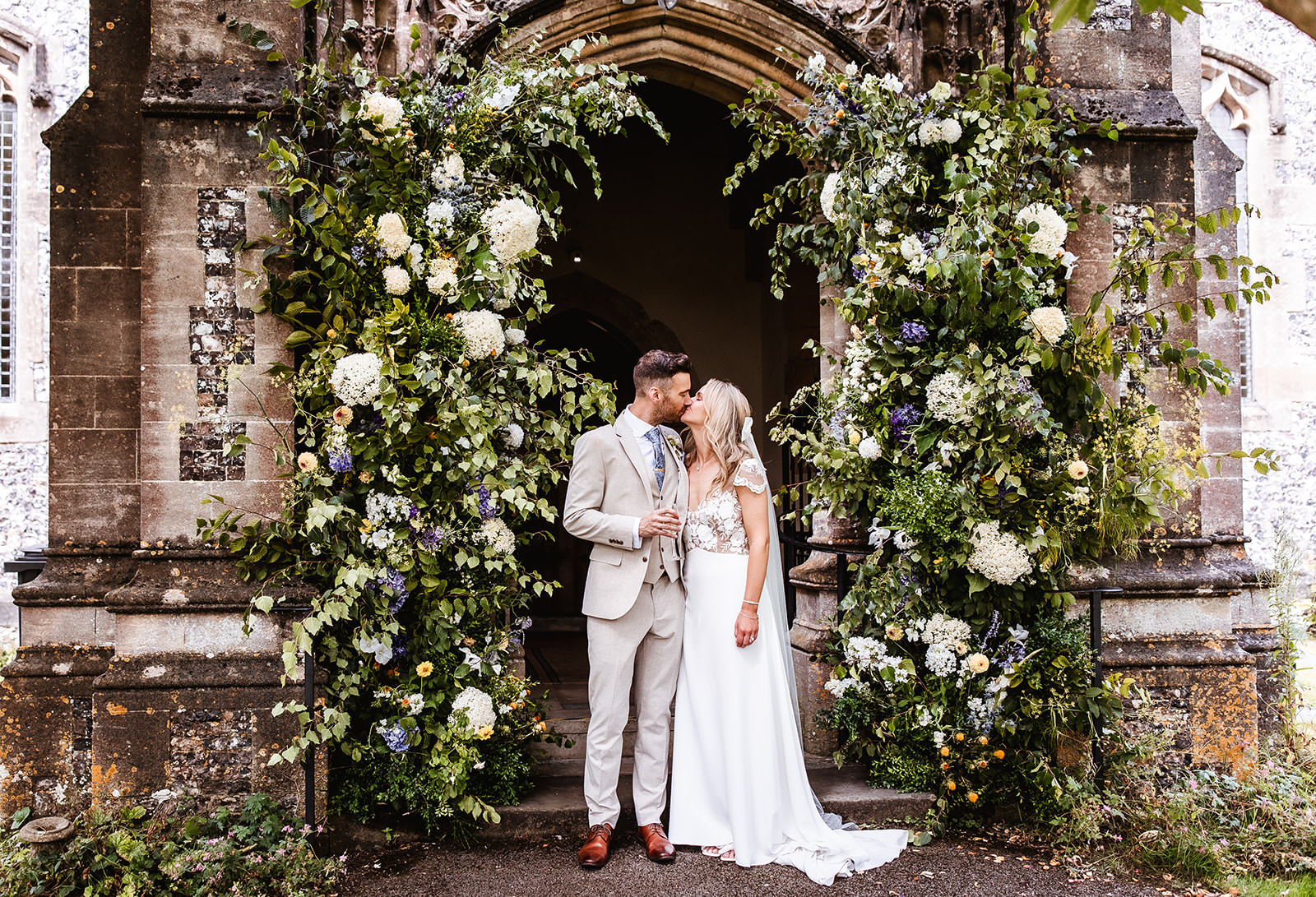 bride and groom kissing at the church by flower arch