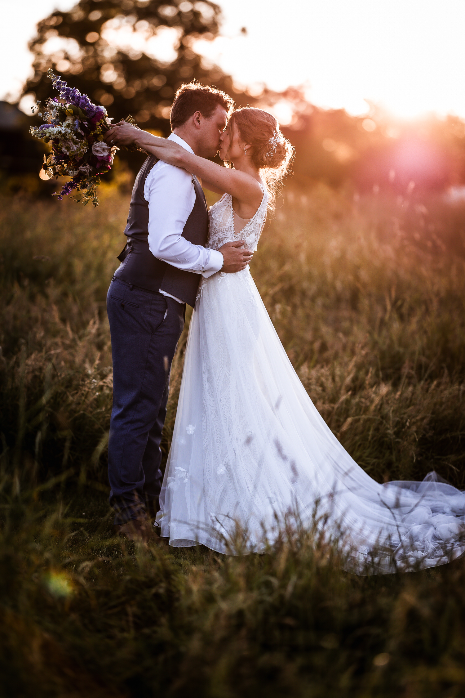 romantic photo of bride and groom cuddling and kissing each other during the sunset in the field