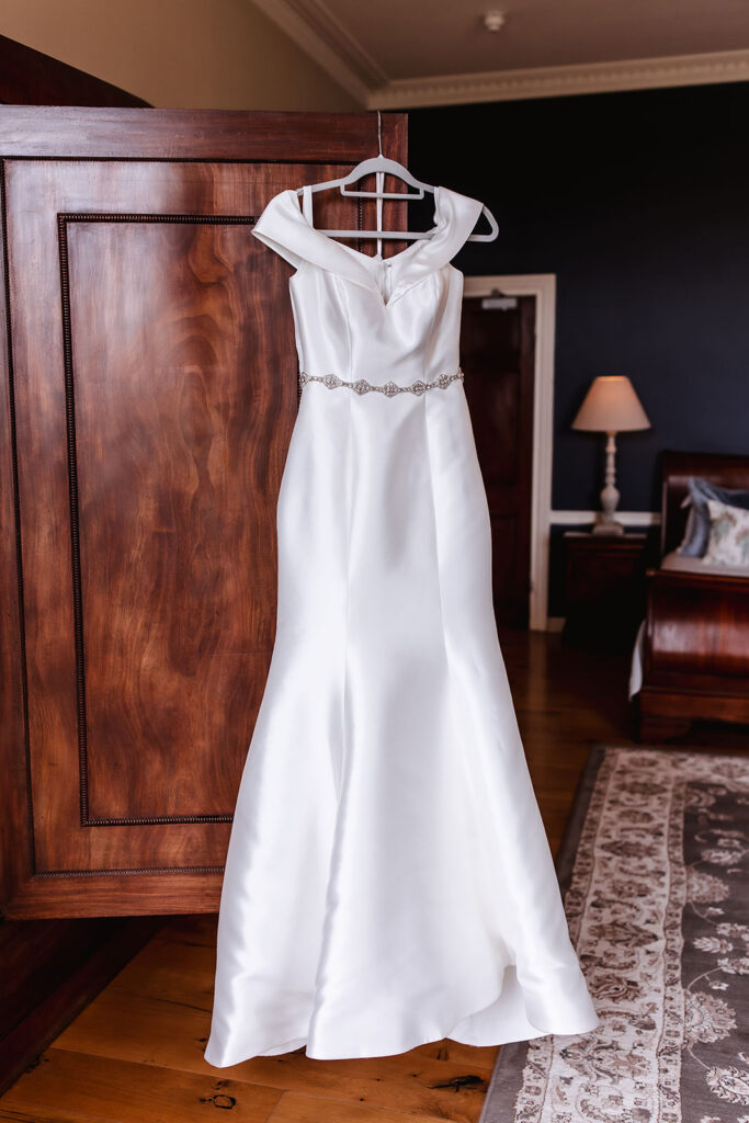 simple and elegant silk wedding dress hanging on the wooden wardrobe at the hotel