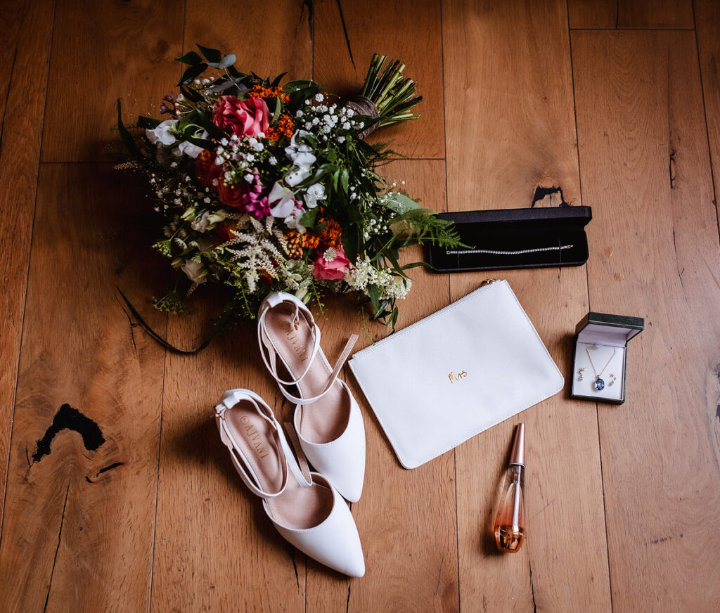 wedding photo of flowers, shoes, perfume, jewelry and wedding invitation on the wooden floor