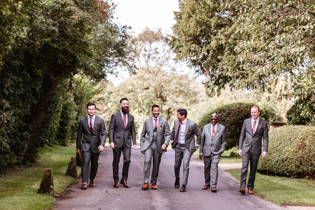 groom is walking with his dad, best friend and groomsmen in the road at Clock Barn, Hampshire