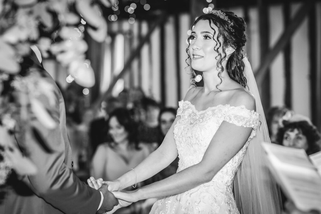 black and white photo of bride holding groom's hands during the ceremony