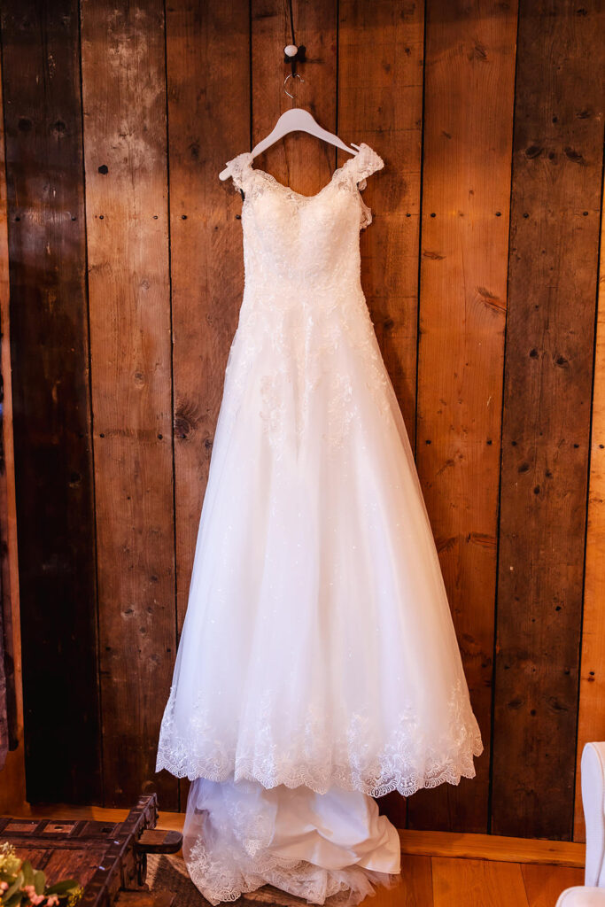 white wedding dress hanging on the hanger in a rustic barn