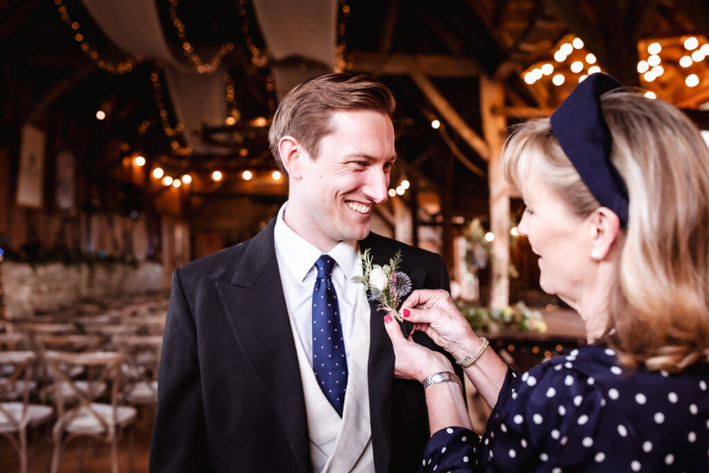 mother of the groom is attaching a wedding button hole flowers on the groom