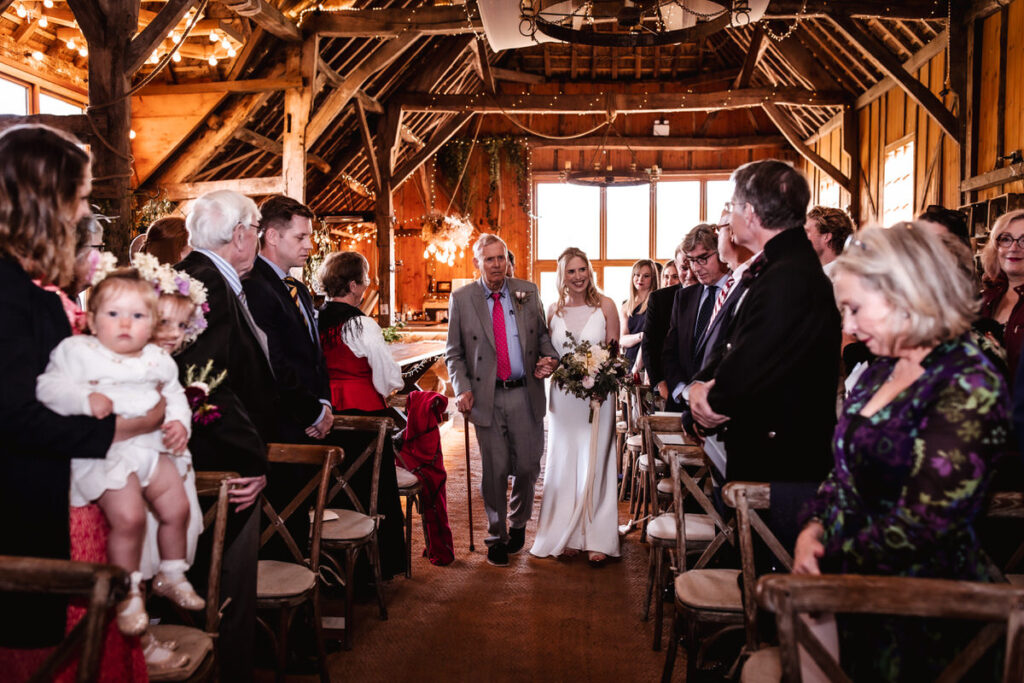 bride and coming down the isle with her father at indoor wedding ceremony at rustic wedding venue in Salisbury, Withshire