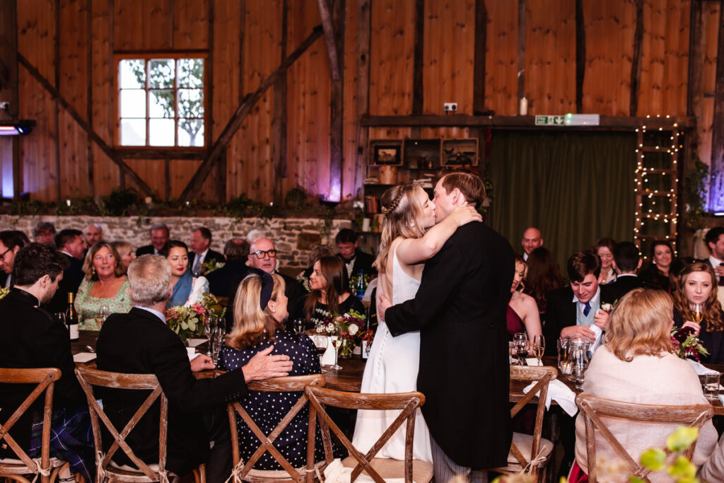 bride and groom are kissing during the wedding reception at rustic barn in Wiltshire