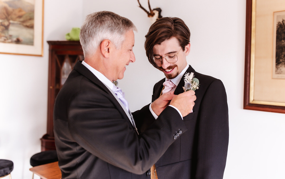 Father is attaching a button hole flowers on the groom