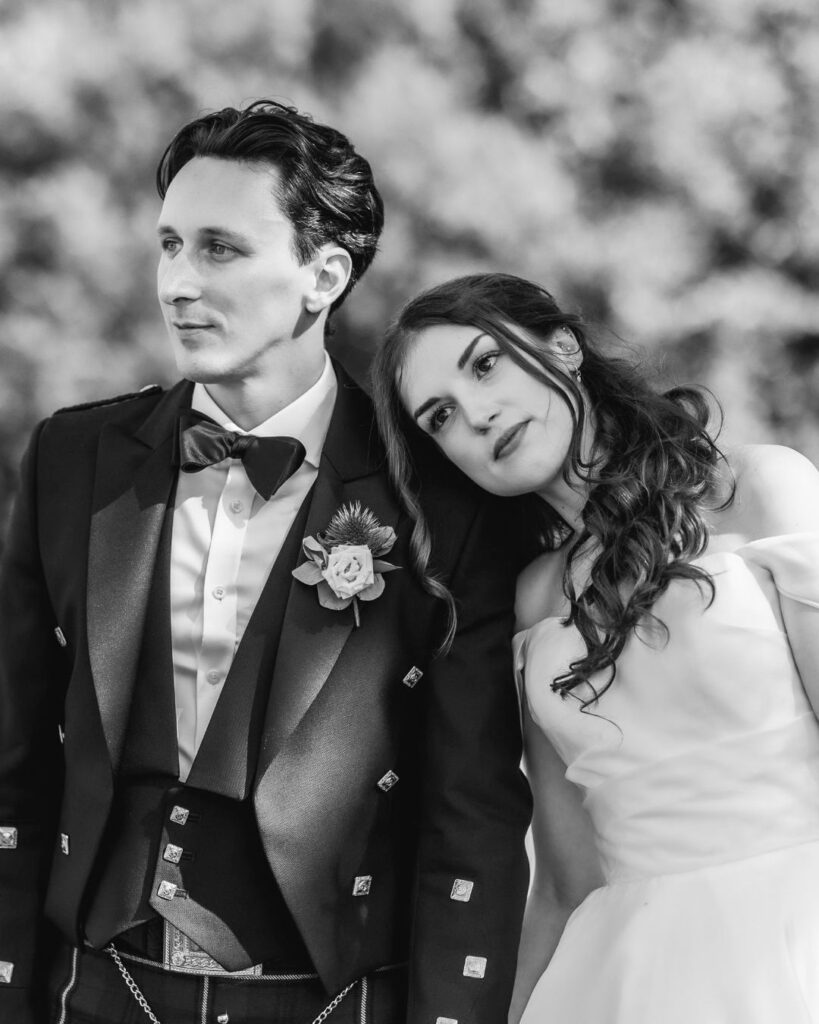 A black and white photo by a Hampshire wedding photographer captures a bride in a strapless gown resting her head on the groom’s shoulder. He wears a formal suit with bow tie and boutonniere as they gaze into the distance, serene and thoughtful.